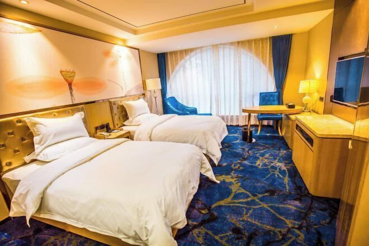 A hotel room with two beds, a desk, a chair, a TV, and a large window with curtains.