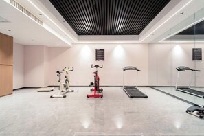 A gym with cardio machines, a treadmill, and a mirrored wall. - Jiang Zhou Hotel (Hengyang)