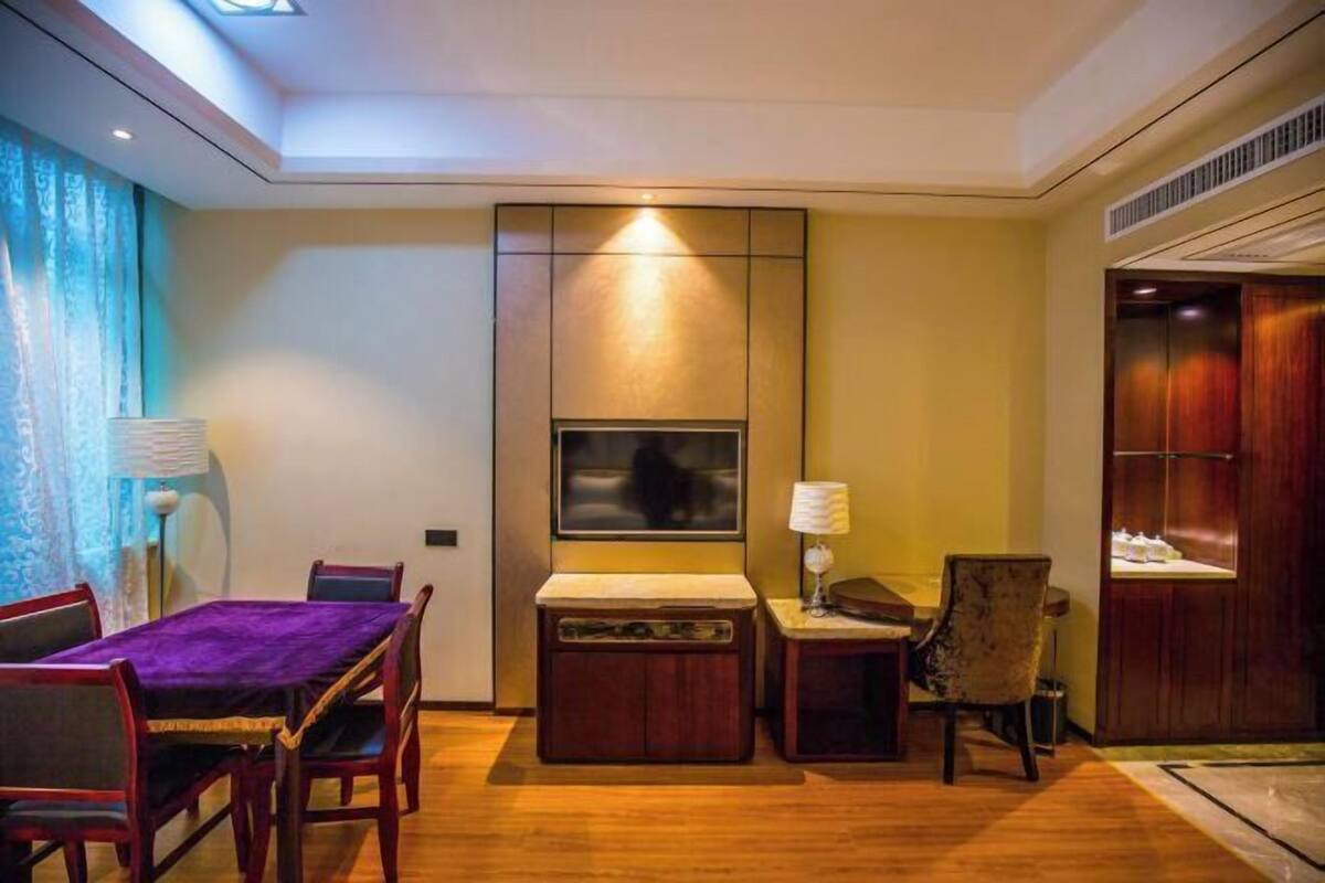 A modern hotel room with a dining area, a TV mounted on the wall, a wooden cabinet, and a wardrobe.