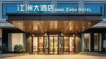 Entrada del Hotel Jiang Zhou con acceso cubierto, puertas de vidrio y un cartel arriba.