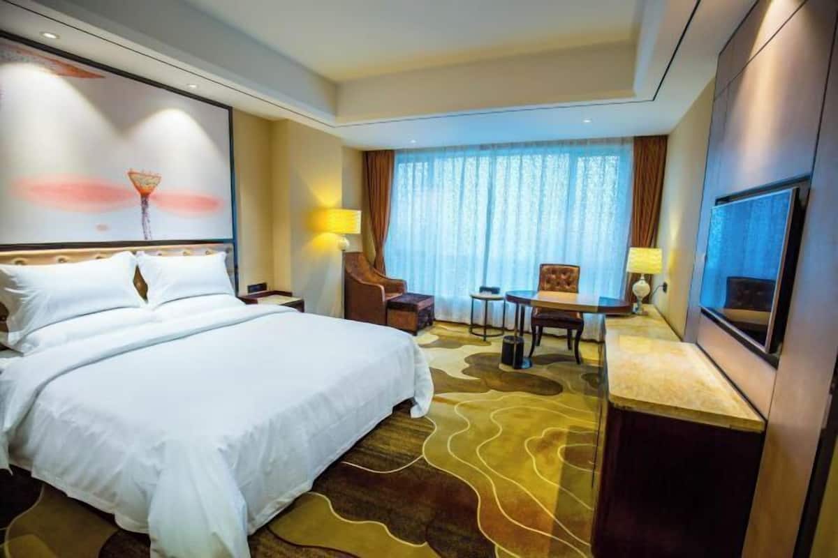 A hotel room with a large bed, a desk, a chair, and a TV.