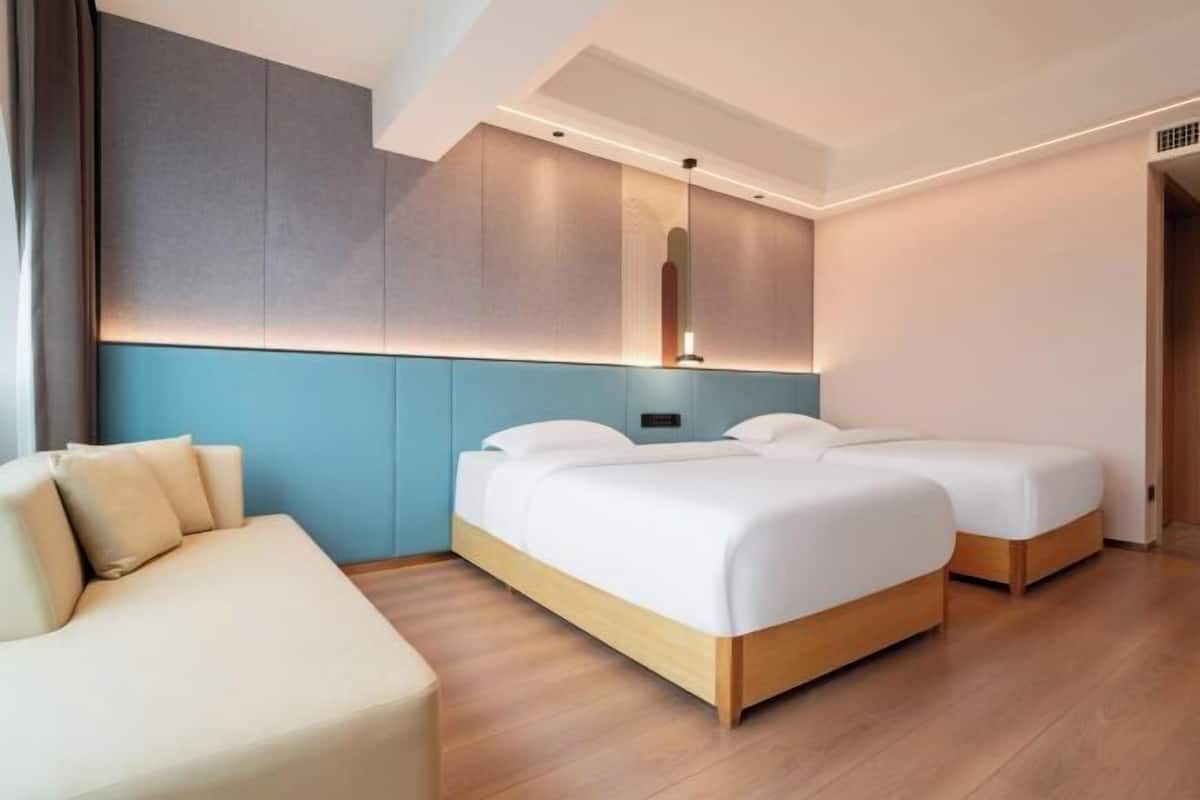 A modern hotel room with a large bed, a sofa, and a wall-mounted mirror.