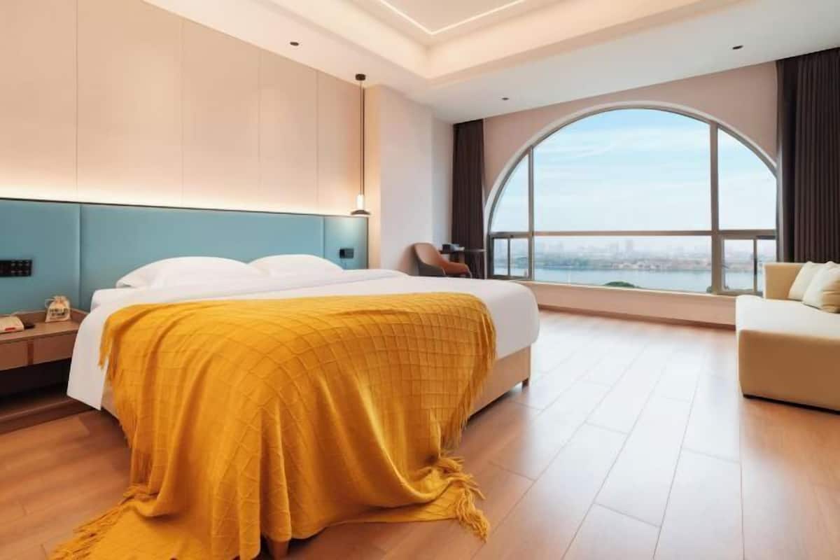 A hotel room with a large bed, a sofa, a view of the city, and a curved window.