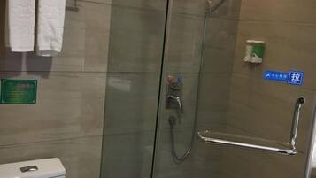 Cabina de ducha con paredes de vidrio, barra de apoyo, perchero con toallas blancas y señal que indica un baño pequeño.