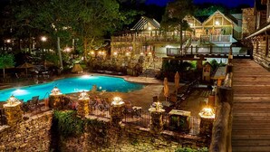 A pool area with a wooden deck, stone walls, and outdoor seating.