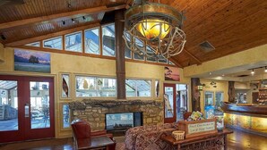 A spacious lobby with a stone fireplace, wooden ceiling, and a large window overlooking the outside.