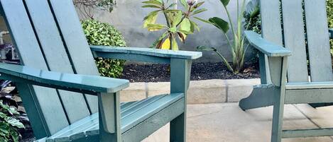 Zwei grüne Adirondack-Stühle mit einem Blumentopf dazwischen auf einer Beton-Terrasse.