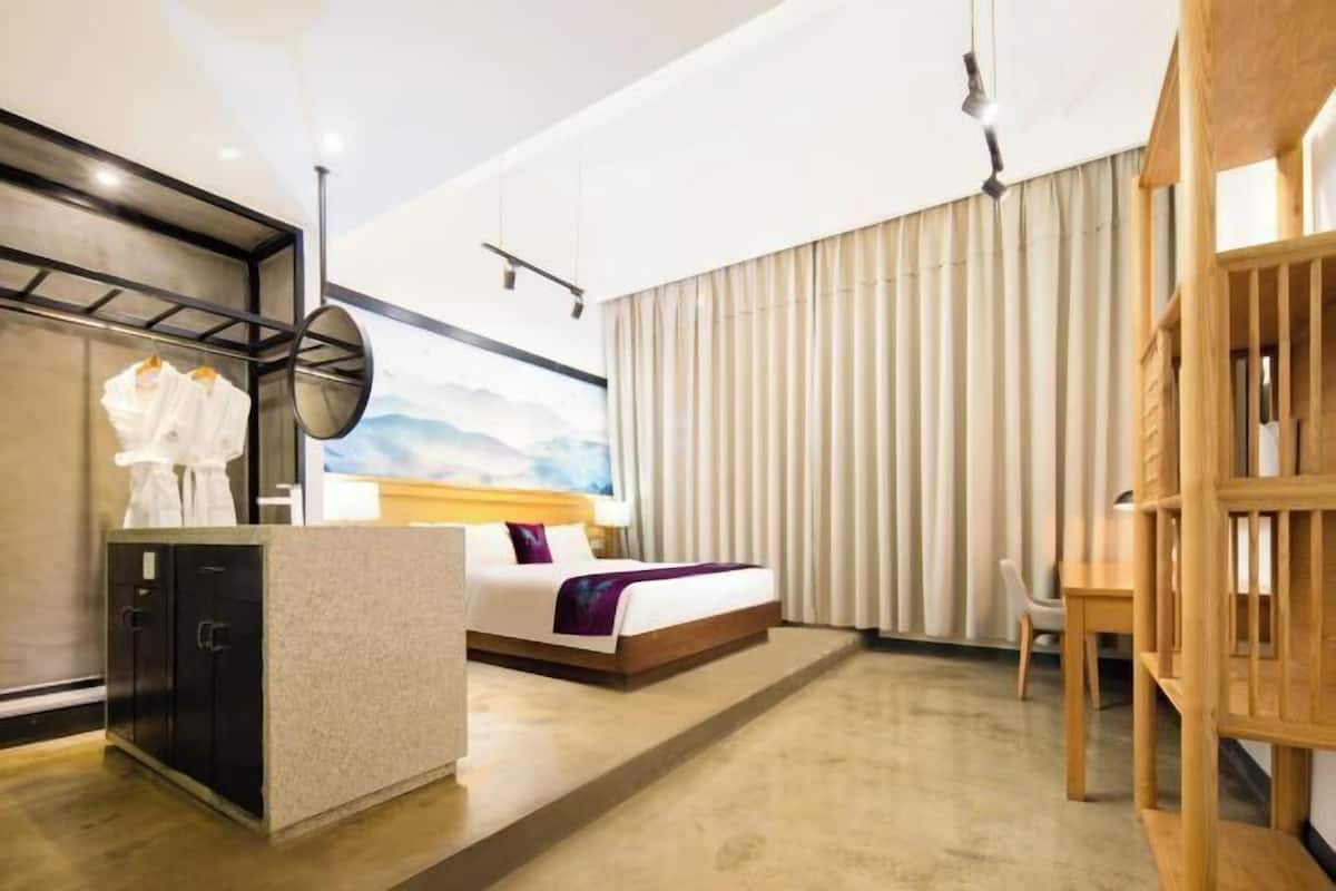 A hotel room with a bed, a desk, a chair, a wardrobe, and a large window with curtains.