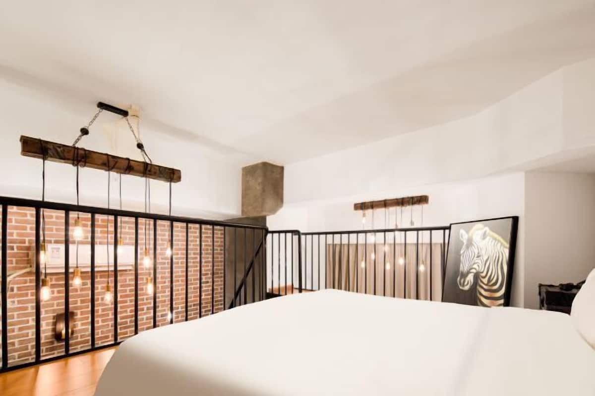 A spacious bedroom with a large bed, a brick wall, a wooden ceiling, and a zebra artwork on the wall.