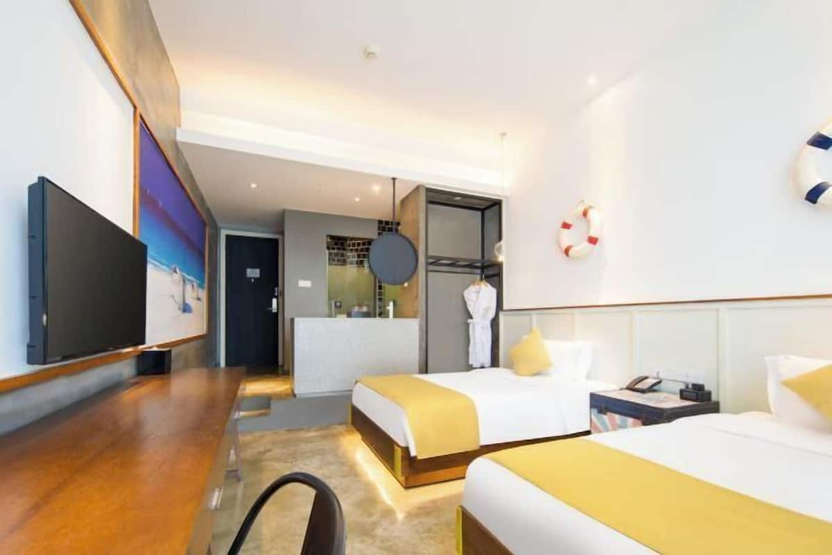 A hotel room with two beds, a desk, a TV, and a bathroom visible in the background.