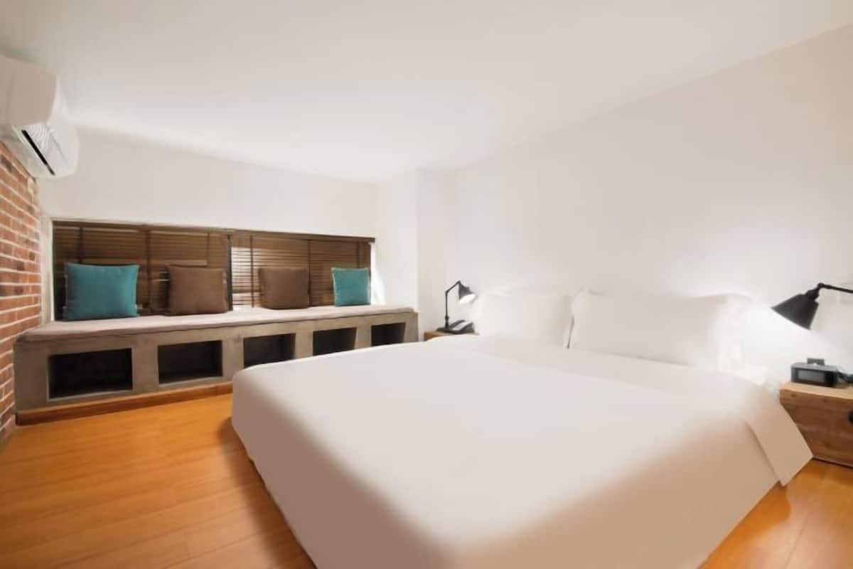 A bedroom with a large bed, a bench with cushions, a nightstand, and an air conditioning unit.