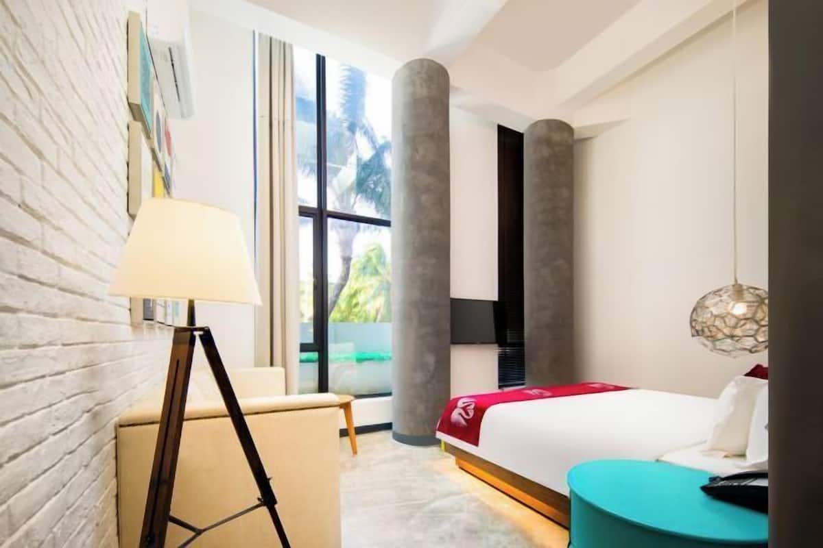 A modern hotel room with a large bed, a desk, a chair, and a view of palm trees through the window.