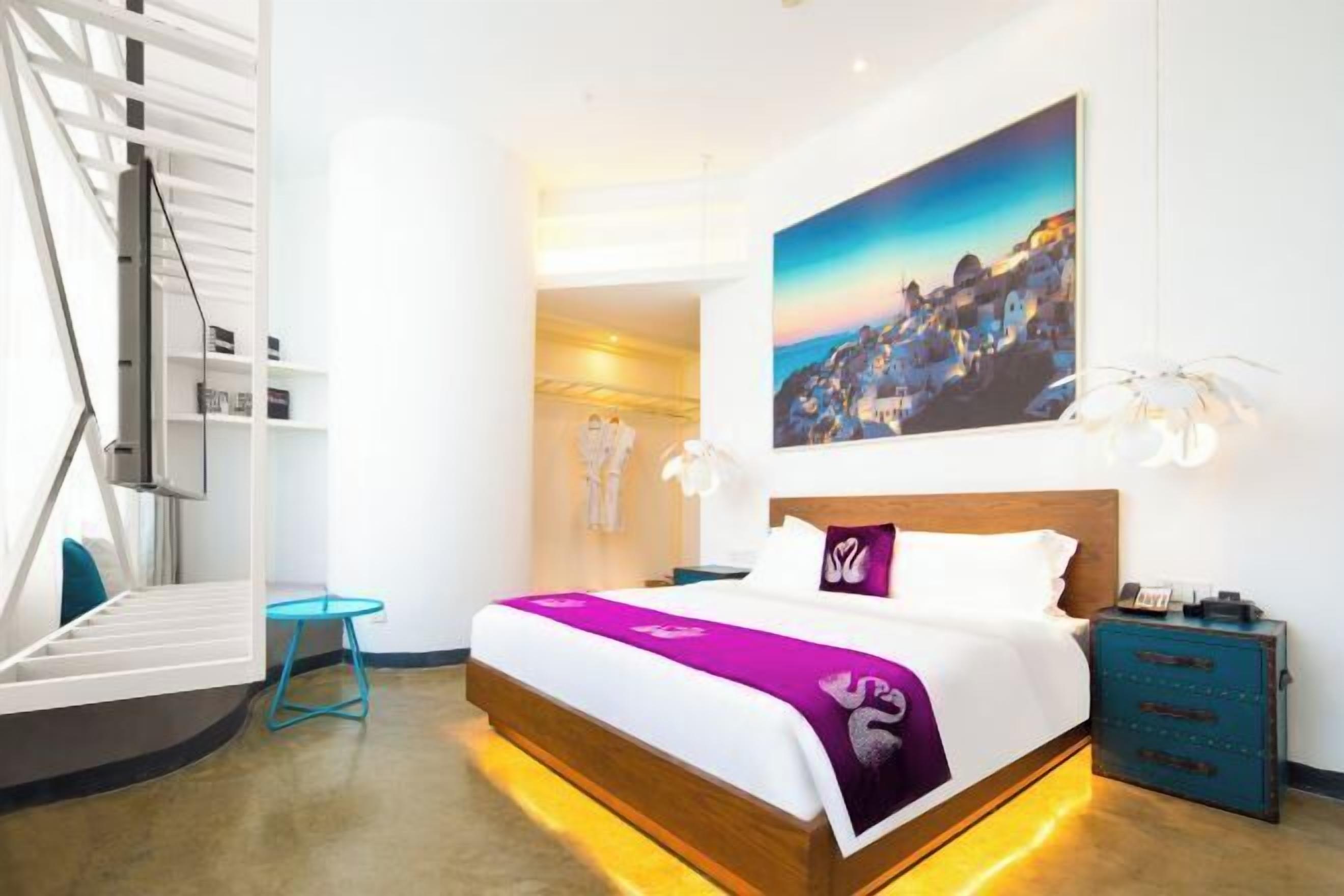 Habitación de hotel moderna con una cama de madera, vistas a un pueblo costero, una mesita y una mesilla de noche.