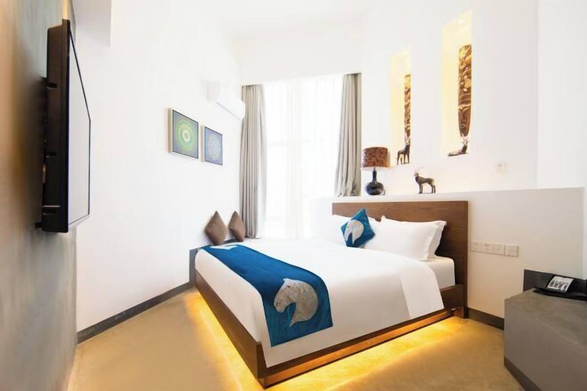 A hotel room with a bed, a TV, a desk, and artwork on the walls.