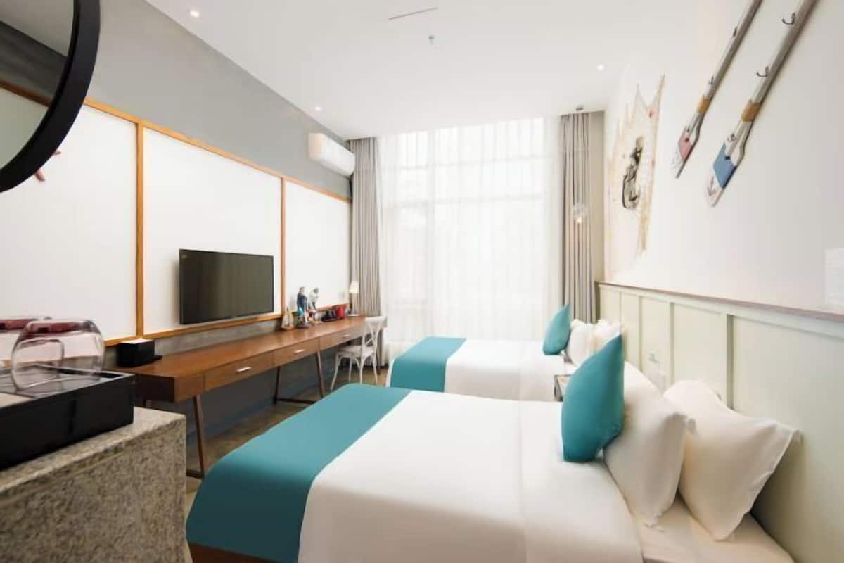A hotel room with two beds, a desk, a TV, and a large window.