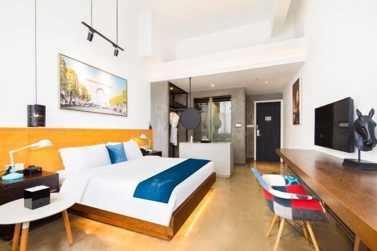 A modern hotel room with a large bed, a desk, a chair, and a television.