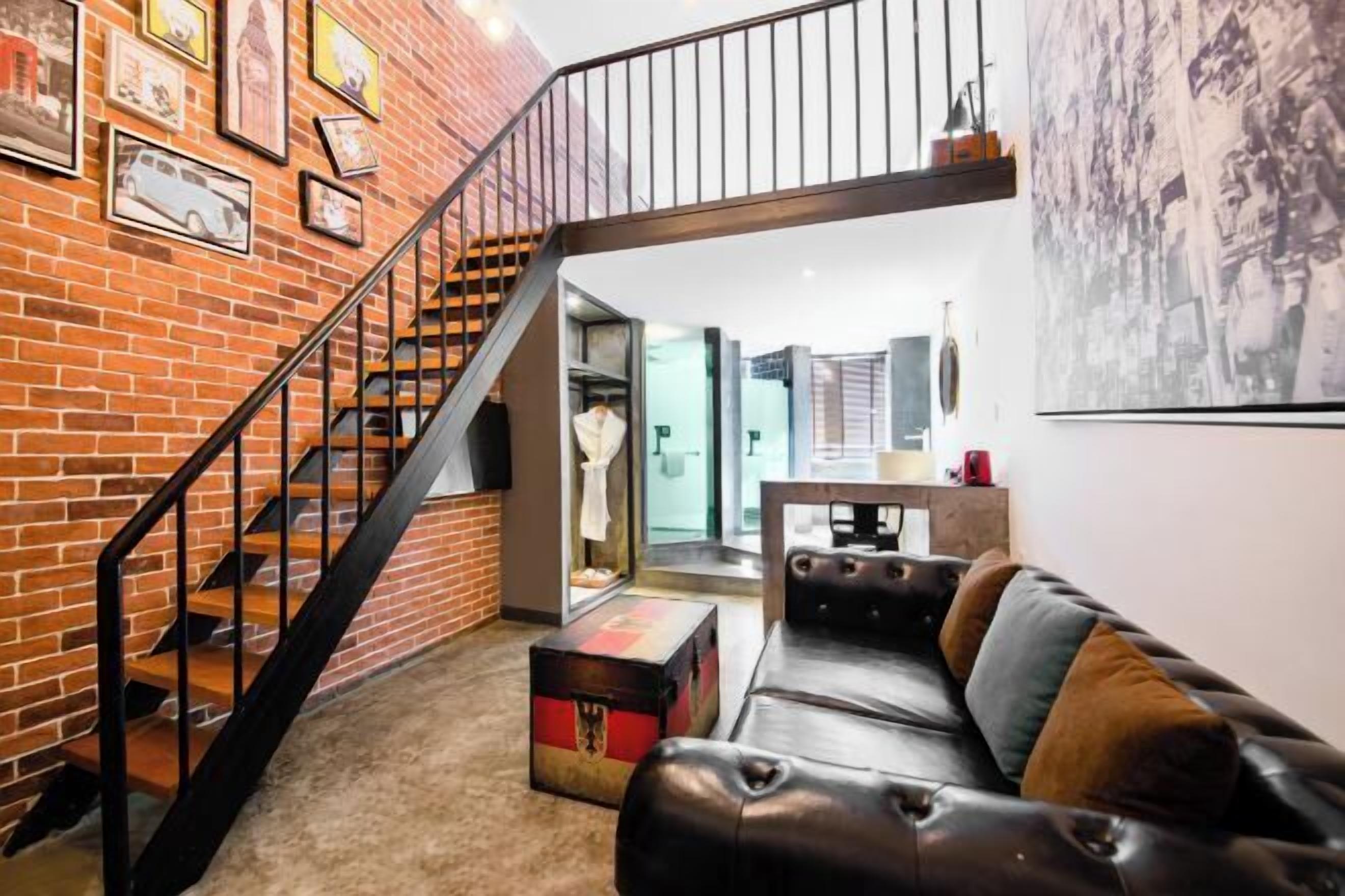 Una sala de estar moderna con pared de ladrillo, un sofá de cuero, una escalera y un cuadro de un paisaje urbano.