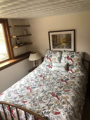 Une chambre à coucher avec une couvre-lit à motifs floraux, un tableau encadré au mur et une lampe de chevet.