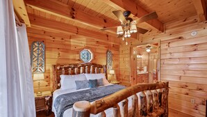 Een slaapkamer in een houten chalet, met een bed, een plafondventilator en een raam met decoratief ontwerp.
