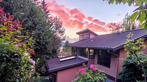 A house with a sloped roof, a covered porch, and a garden with various plants and flowers. - Modern Hillhouse with Lake Washington Views (Kirkland)