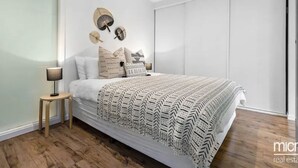 Quarto moderno com uma cama grande, mesa de cabeceira e ventoinha fixada na parede.