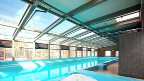Piscina no terraço com teto de vidro, hidromassagem e vista da cidade.
