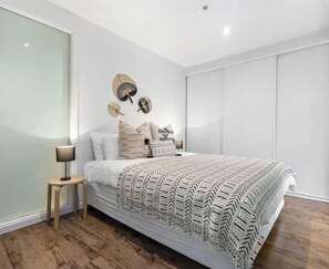 A modern bedroom with a large bed, a bedside table, and a wall-mounted fan.