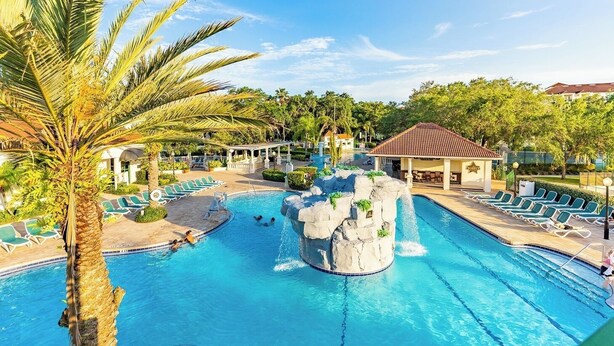 A resort pool with a waterfall feature, lounge chairs, and a covered pavilion. - Kissimmee | Family Park Trip | Pool & Sports Courts | 3BR Sleeps 8 (Kissimmee)
