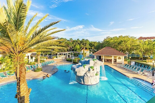 Piscina de resort con cascada, sillas de descanso y pabellón cubierto.
