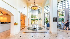 A hotel lobby with a reception desk, a chandelier, a fountain, and a sign listing amenities. - Kissimmee | Family Park Trip | Pool & Sports Courts | 3BR Sleeps 8 (Kissimmee)