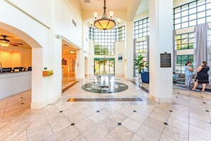 Vestíbulo de hotel con recepción, una araña, una fuente y un cartel que enumera los servicios.