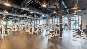 A spacious gym with various exercise machines, large windows, and hanging pendant lights. - Kissimmee | Family Park Trip | Pool & Sports Courts | 3BR Sleeps 8 (Kissimmee)
