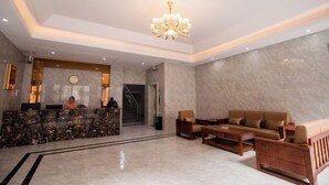 A lobby with a reception desk, a chandelier, a staircase, and seating area. - Feng Huang Business Hotel (Luxi)