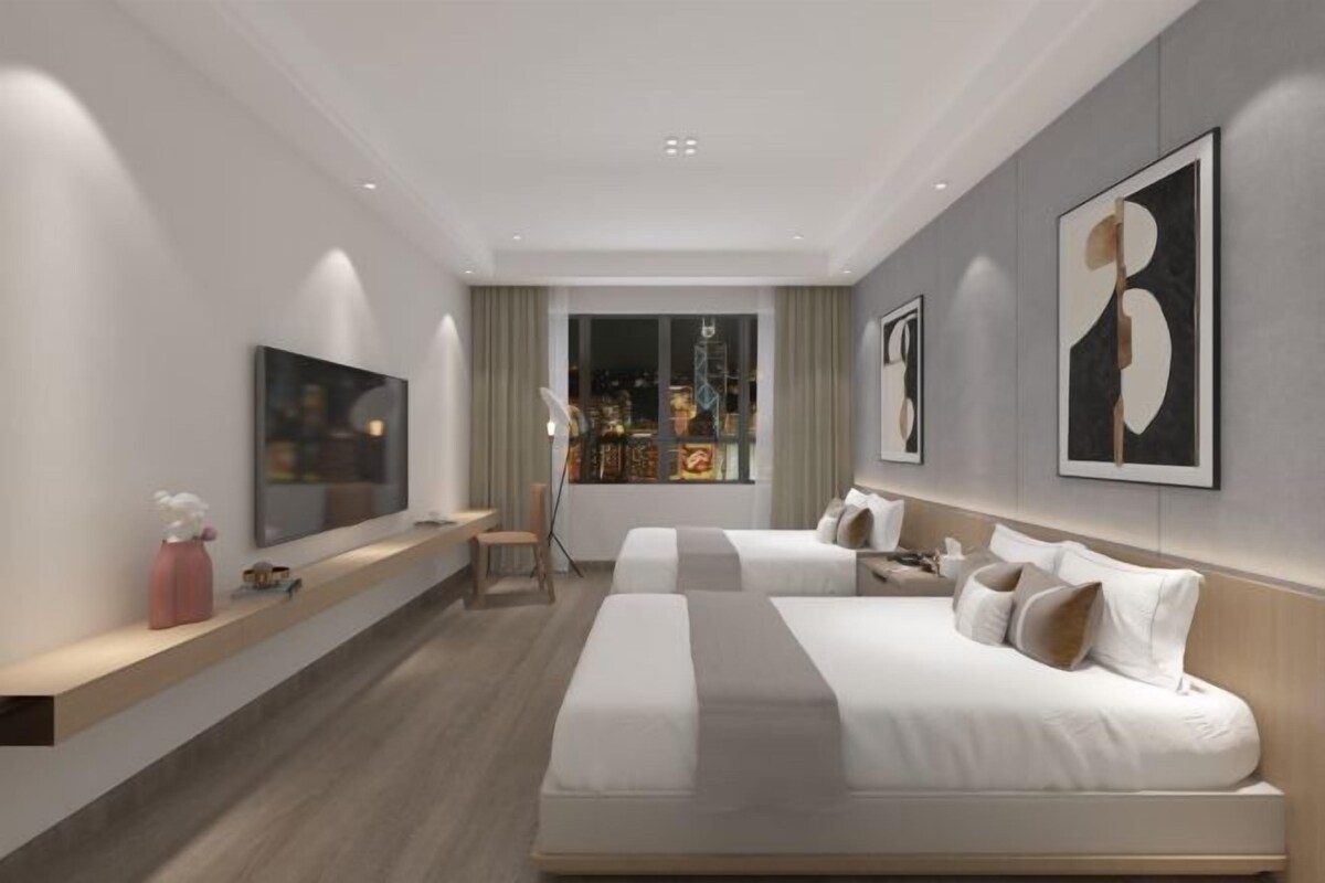 A modern hotel room with two beds, a TV, artwork, and a window with a city view.