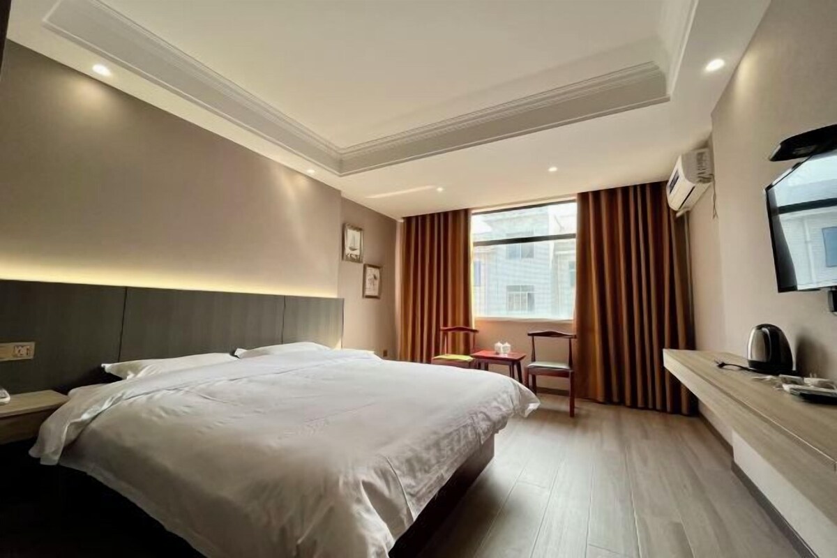 A hotel room with a large bed, a desk, a chair, a TV, and a window with curtains.
