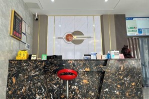 A reception desk with a marble counter, a clock, and a digital screen displaying information. - Feng Huang Business Hotel (Luxi)