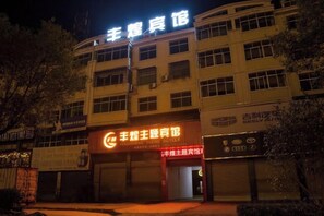 A building with multiple floors, a prominent sign at the top, and several ground-level commercial establishments. - Feng Huang Business Hotel (Luxi)