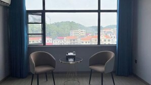 A room with a large window, two chairs, and a small table. - Feng Huang Business Hotel (Luxi)
