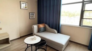 A modern room with a sofa, a small round table, and a window with curtains. - Feng Huang Business Hotel (Luxi)
