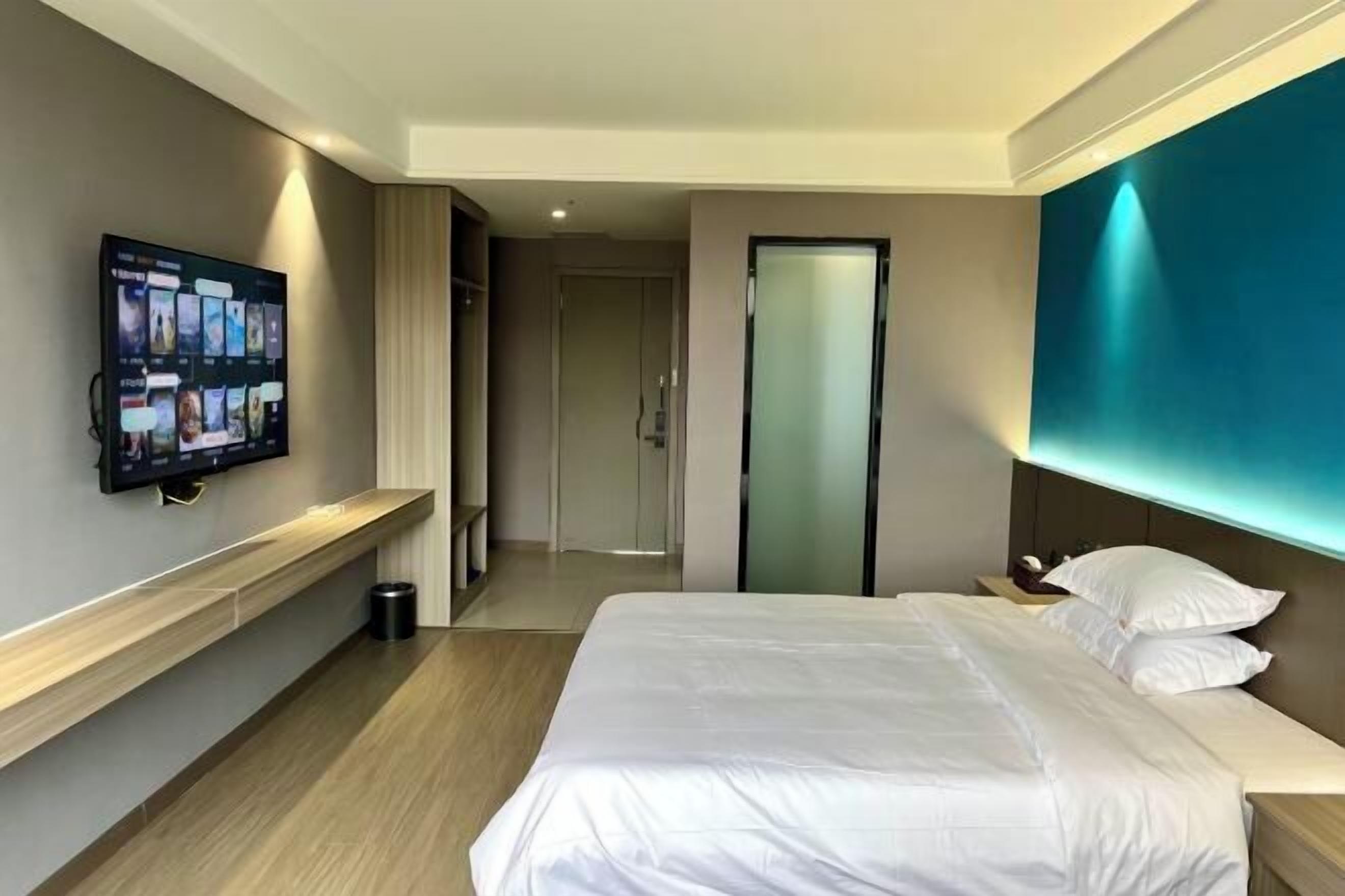 A hotel room with a bed, a TV mounted on the wall, a bedside table, and a nightstand.