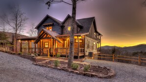 Un'ampia baita di legno con un portico sporgente, numerose finestre e facciata ben illuminata.