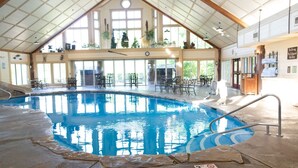 Une piscine intérieure dotée d’un haut plafond, de grandes fenêtres et d’un espace détente avec des tables et des chaises.