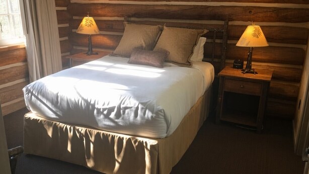 Une chambre à coucher de style cabane en bois, avec un lit, deux lampes de chevet et une fenêtre avec des rideaux.