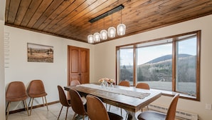 A dining area with a wooden table, brown chairs, a wooden ceiling, and a large window with a view of hills. - Tranquil Lodge with A+ Amenities (Naples)
