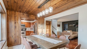 A dining area with a wooden table and chairs, a kitchen in the background, and a living room with a sofa and TV. - Tranquil Lodge with A+ Amenities (Naples)