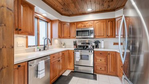 A modern kitchen with wooden cabinets, stainless steel appliances, and a black rug. - Tranquil Lodge with A+ Amenities (Naples)