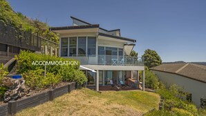 Uma casa moderna de dois andares com varanda, um pátio com cadeiras e área de jardim.