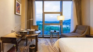 A hotel room with a bed, a desk with a lamp, a chair, and a view of a body of water. - Hui Chang Hotel (Huichang)