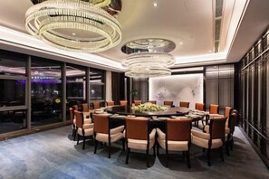 Un comedor moderno con una mesa redonda rodeada de sillas, grandes candelabros y vistas a la ciudad a través de amplios ventanales.