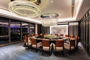 Un comedor moderno con una mesa redonda rodeada de sillas, grandes candelabros y vistas a la ciudad a través de amplios ventanales.